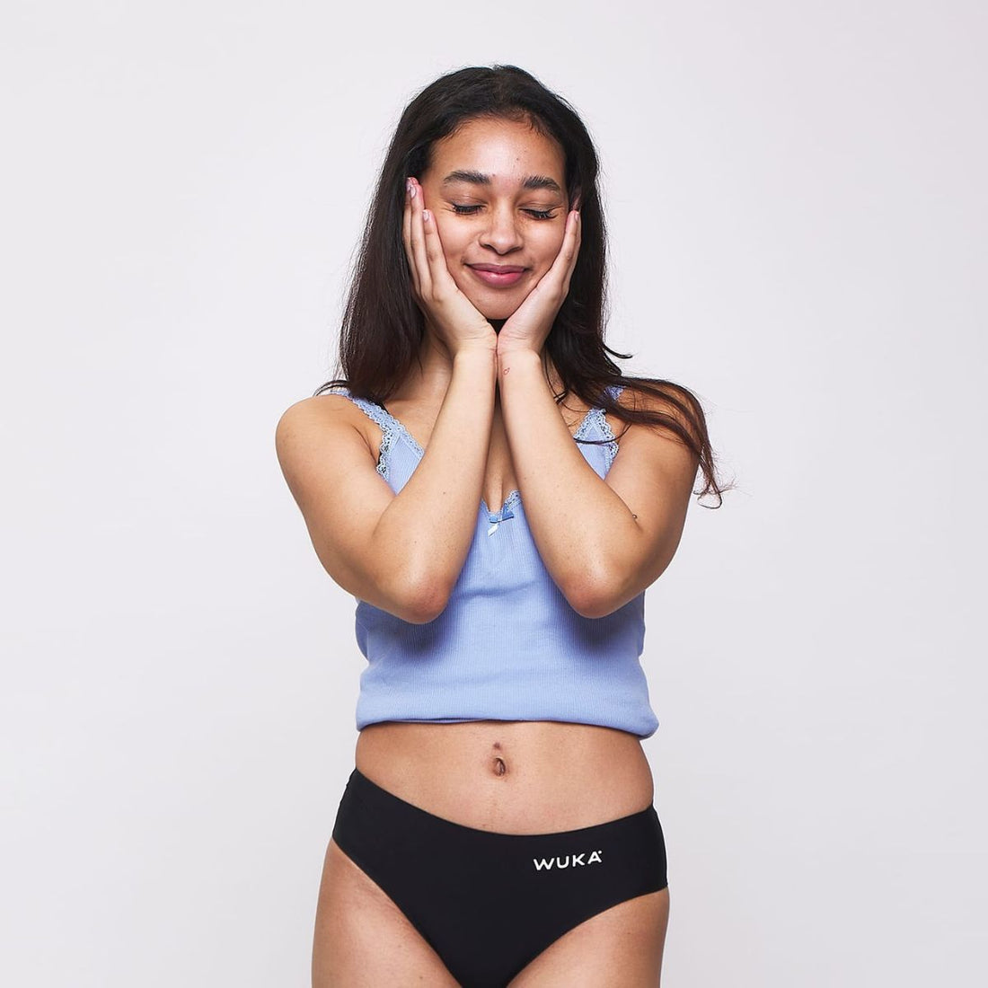 Teen girl in WUKA period pants gently holding her face with a smile—feeling calm, confident, and totally in tune with her body during her cycle.